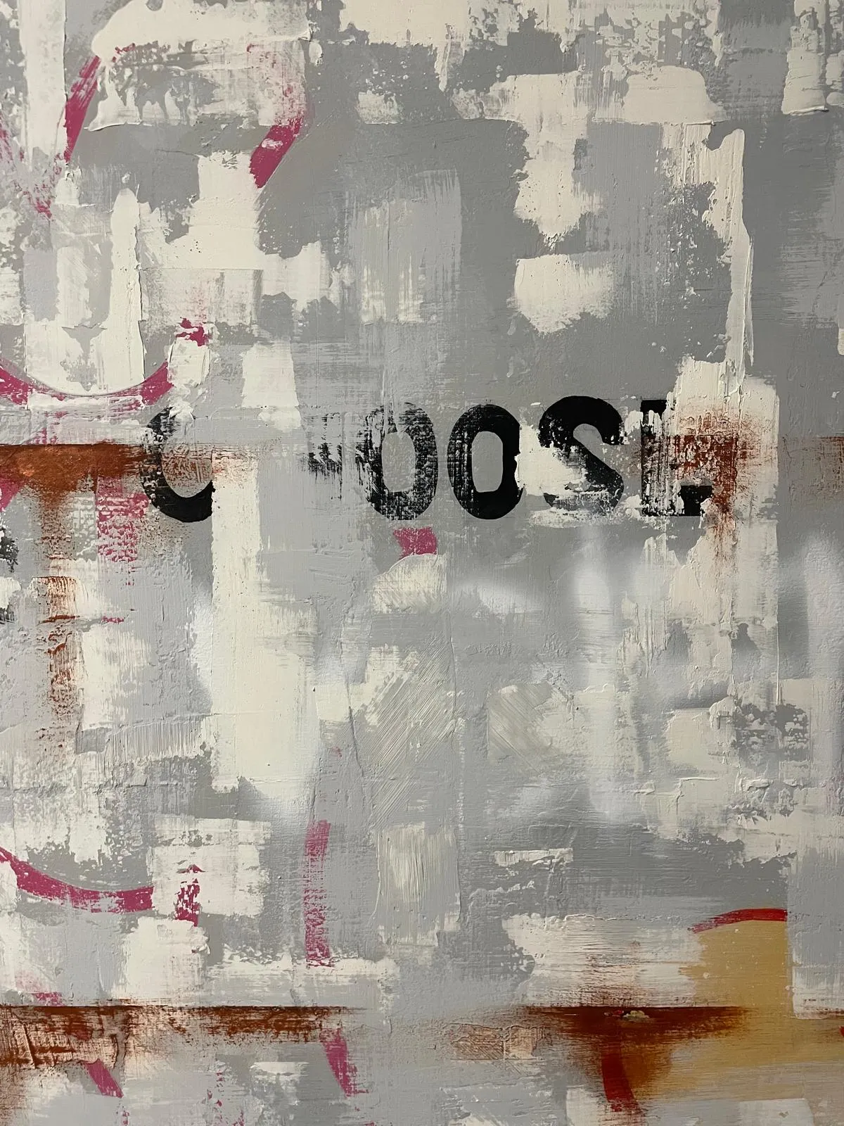 Detail of the wall: the word CHOOSE in black stencil letters, partly painted over by grey and white brushmarks, with magenta flecks and a rust-coloured band beneath.