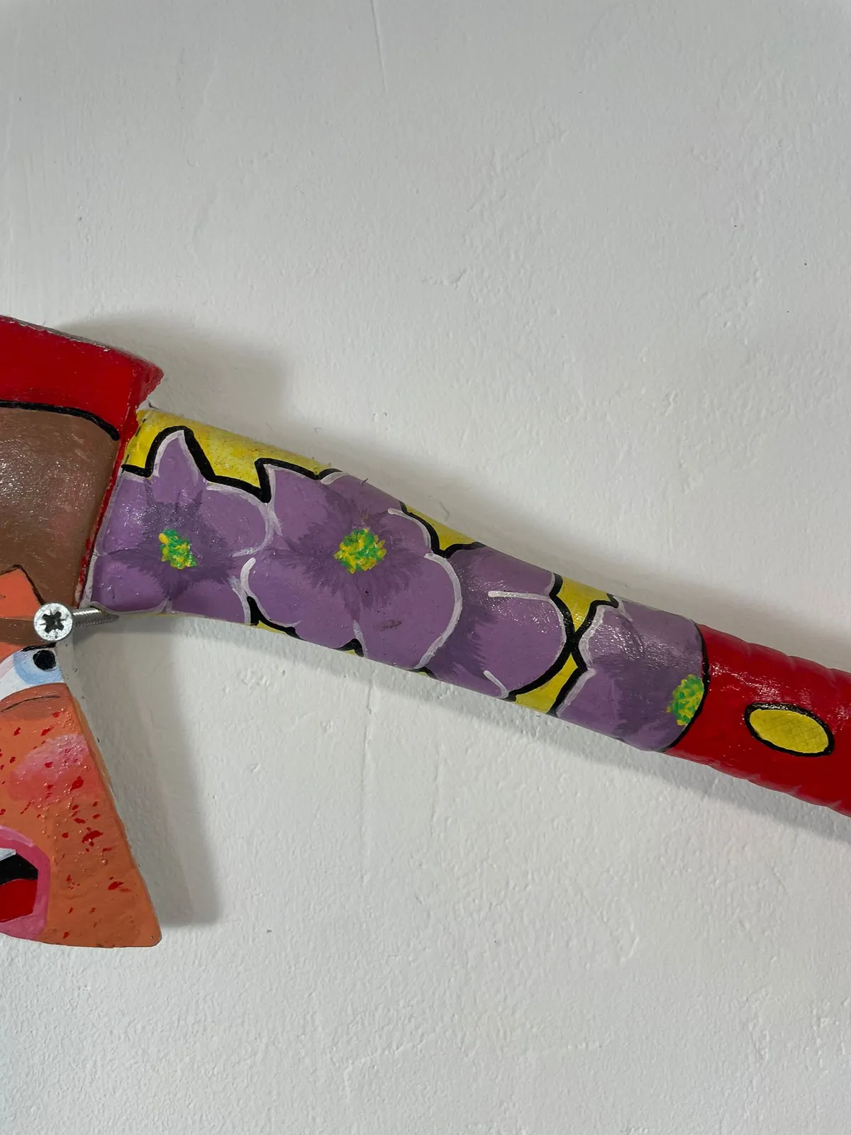 Detail of the handle: purple flowers with green centres on a yellow ground, running from the red collar down towards the grip, with the painted face cropped at the left edge.